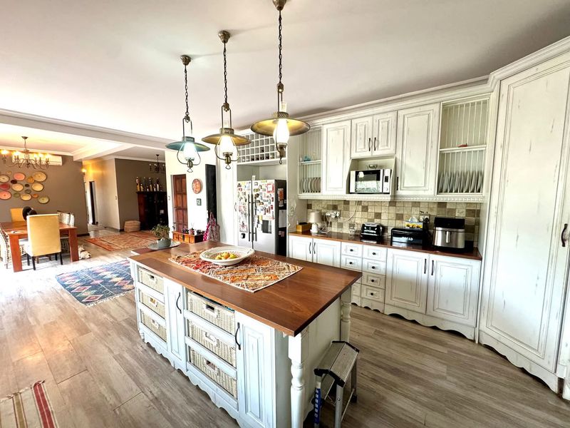 Spacious open-plan kitchen featuring a central timber-topped island, classic white cabinetry, tiled backsplash, and warm pendant lighting, seamlessly flowing into the dining area.
