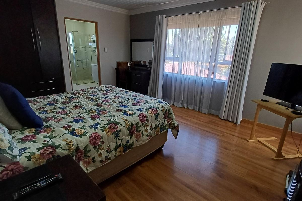 Spacious bedroom featuring wood-look flooring, built-in cupboards, and an en-suite bathroom with a glass-enclosed shower.