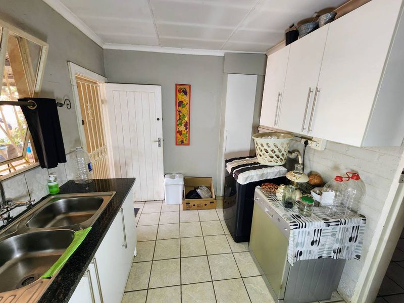 A functional scullery area featuring a double bowl stainless steel sink, granite countertops, and built-in cabinetry with tiled flooring.