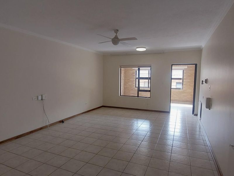 Spacious, empty living area featuring neutral tiled flooring, a ceiling fan, and natural light through aluminium-framed windows leading to an outdoor space.