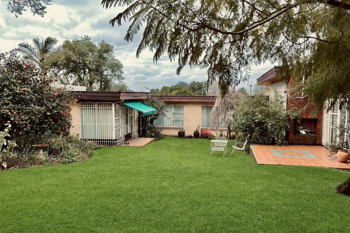 A spacious rear garden featuring a well-maintained lawn, a tiled patio area, and a built-in outdoor fireplace, providing a private outdoor living space.