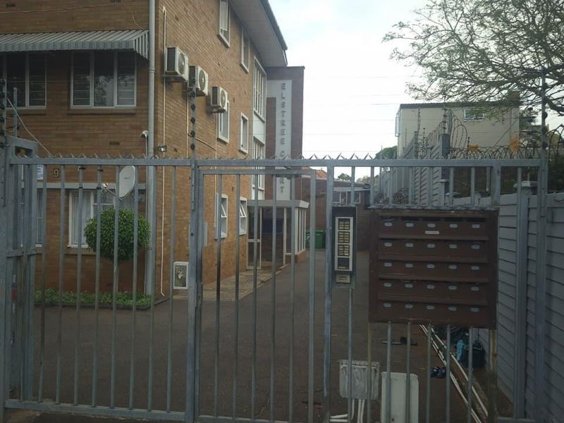 Front view of the apartment complex entrance featuring a secure metal gate, intercom system, mailboxes, and brick building facade.