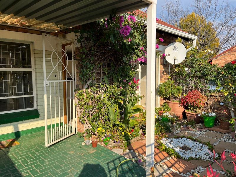 A covered patio area featuring a security gate, brick paving, and a satellite dish, set within a landscaped garden space.