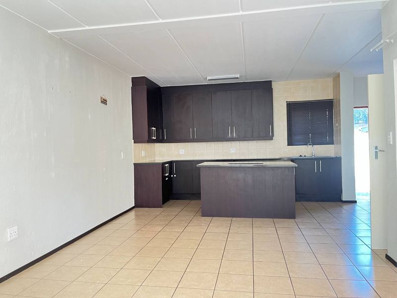 An open-plan kitchen featuring dark wood cabinetry, a central island, tiled flooring, and a tiled backsplash in a clean, vacant space.