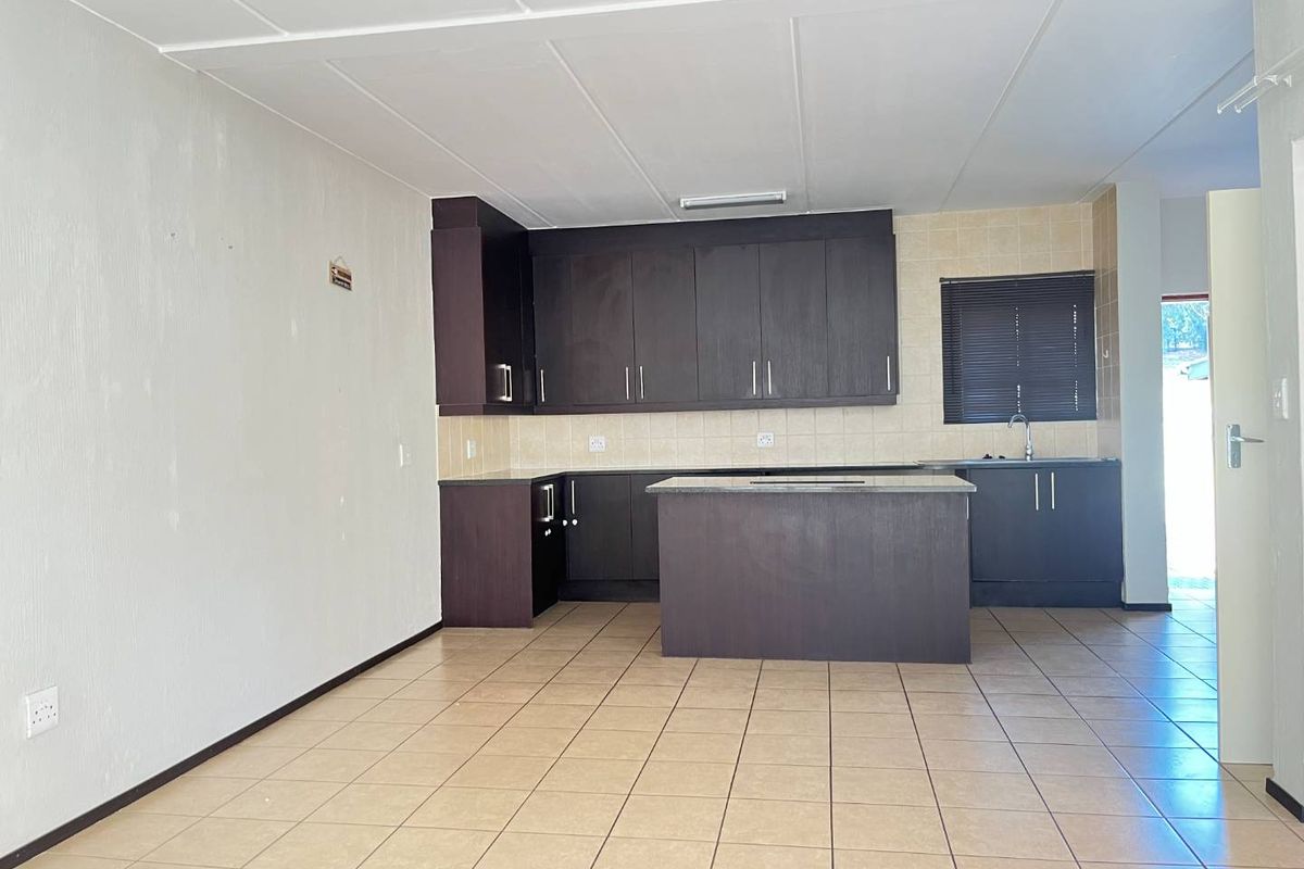 An open-plan kitchen featuring dark wood cabinetry, a central island, tiled flooring, and a tiled backsplash in a clean, vacant space.