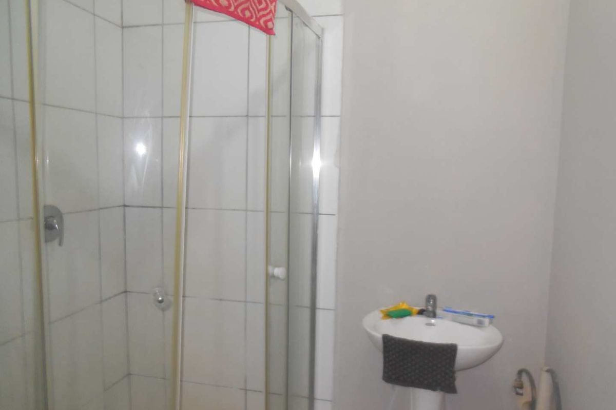 A functional bathroom featuring a corner shower enclosure with tiled walls and a white pedestal basin.