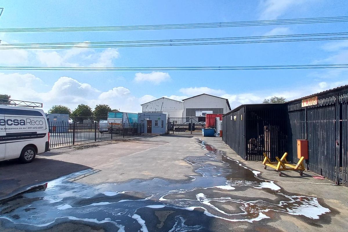 Industrial yard area featuring paved surfacing, perimeter metal fencing, and access to storage or workshop units.