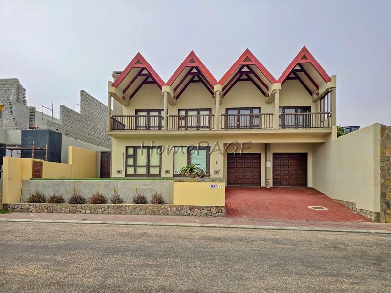 A modern double-story residential property featuring a distinctive gabled roof design, a double garage, and an upper-level balcony with a paved driveway.