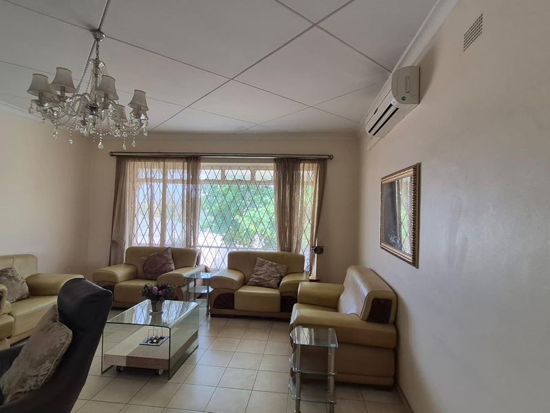A living room featuring tiled flooring, a split-system air conditioner, and a decorative chandelier, with security gates on the windows.