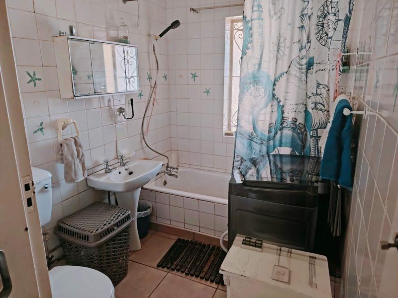 A compact bathroom featuring a pedestal basin, toilet, and a combined shower-bathtub unit with tiled finishes.