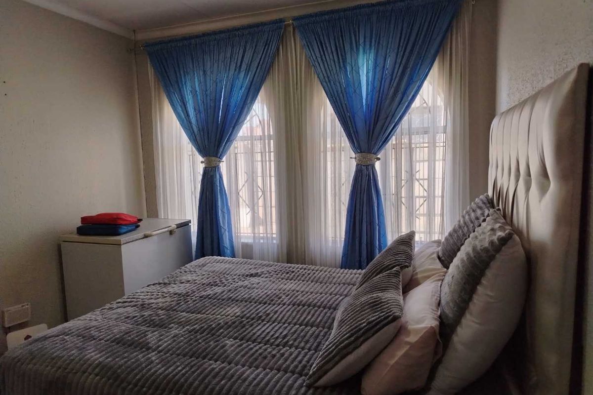A comfortable bedroom featuring large windows with security bars and decorative curtain treatments.
