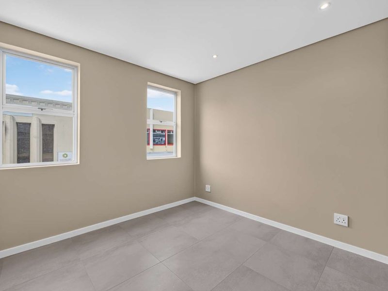 A bright, empty bedroom featuring neutral walls, modern grey floor tiles, recessed lighting, and a built-in wardrobe.