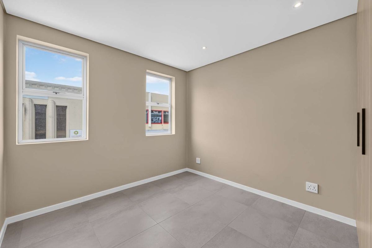 A bright, empty bedroom featuring neutral walls, modern grey floor tiles, recessed lighting, and a built-in wardrobe.
