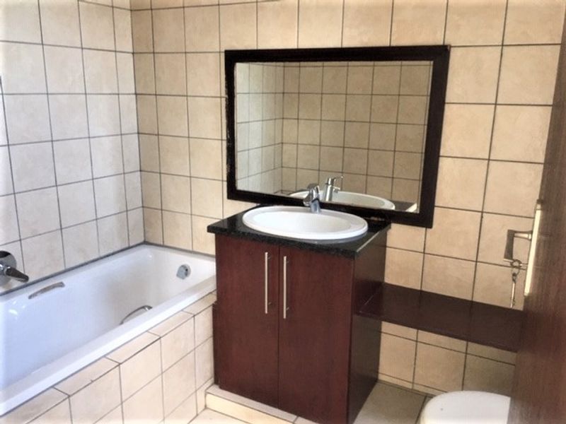A functional bathroom featuring a built-in vanity with a ceramic basin, a bathtub, and neutral wall tiling throughout.