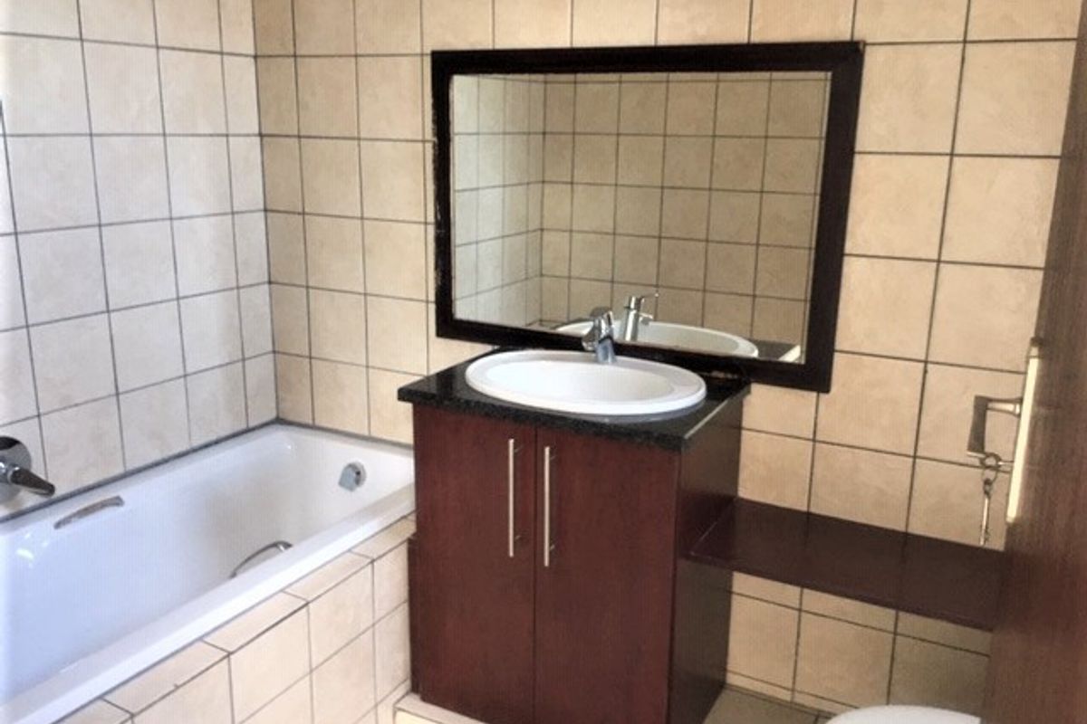 A functional bathroom featuring a built-in vanity with a ceramic basin, a bathtub, and neutral wall tiling throughout.