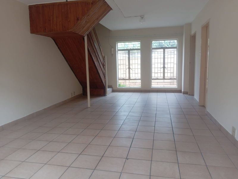 An empty, open-plan living area featuring tiled flooring and a prominent wooden staircase, offering a blank canvas for interior design.
