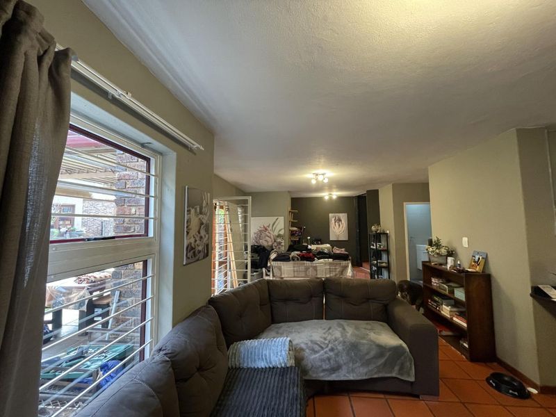 Open-plan living area featuring terracotta floor tiles, neutral wall tones, and large windows with security bars, offering a functional and connected layout.