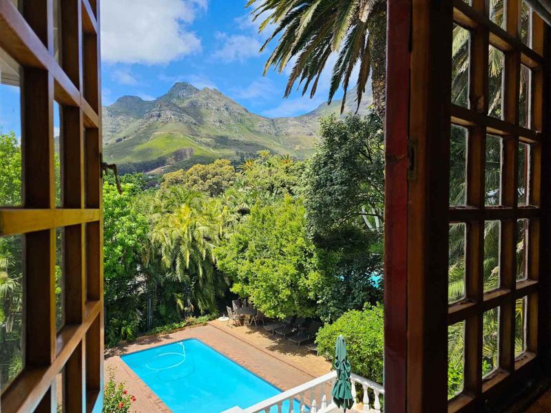 A scenic elevated view overlooking a private swimming pool and lush garden, framed by traditional timber window frames with a mountain backdrop.