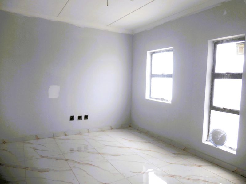 A bright, empty bedroom featuring modern marble-look tiled flooring, neutral walls, and large aluminium-framed windows, ready for personalization.
