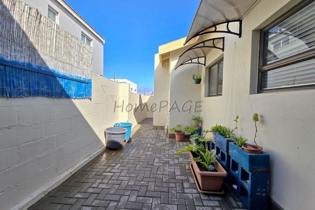 A paved rear courtyard area featuring a boundary wall, exterior windows, and fitted awnings, providing a functional outdoor space for the townhouse.