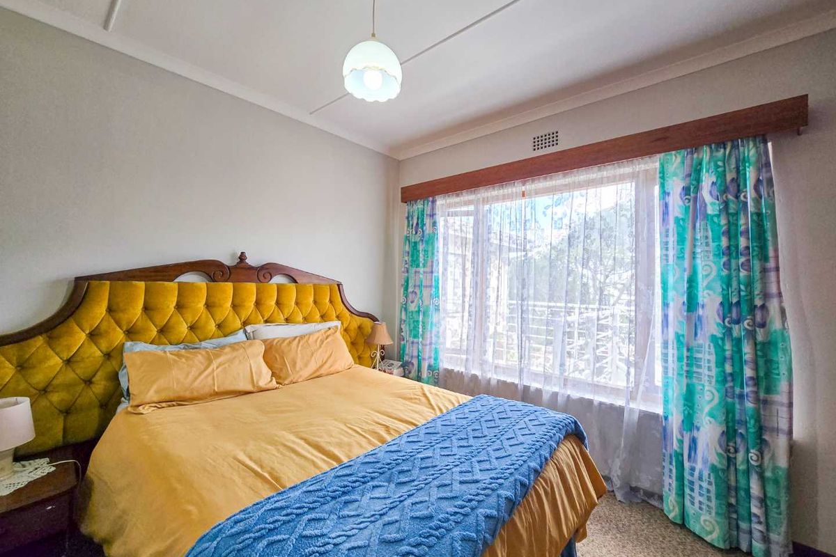 A bedroom featuring a large window with timber pelmet, neutral wall finishes, and a central pendant light fixture.