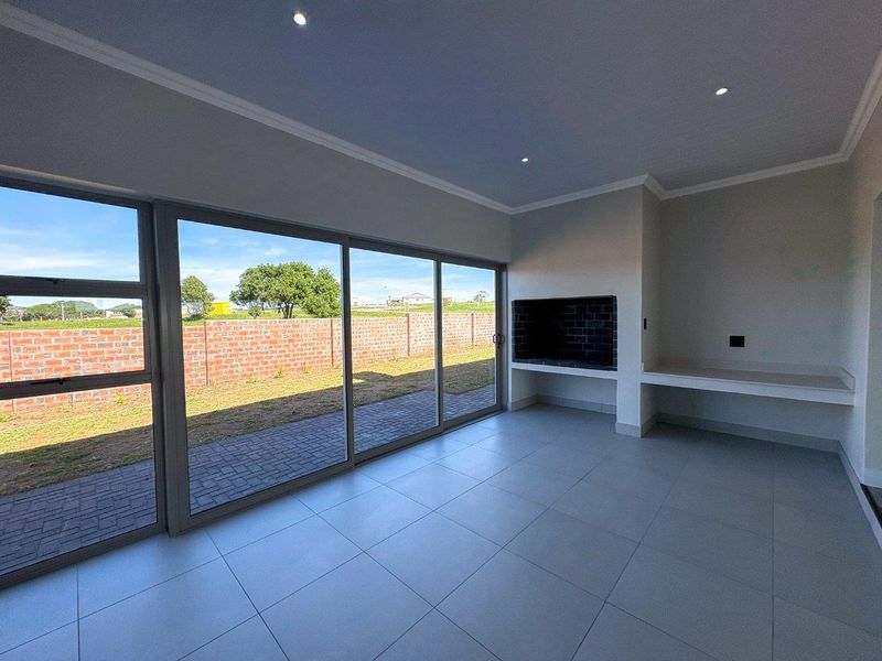 A modern, empty indoor patio area featuring large sliding glass doors, a built-in braai, and sleek tiled flooring, perfect for outdoor entertaining.