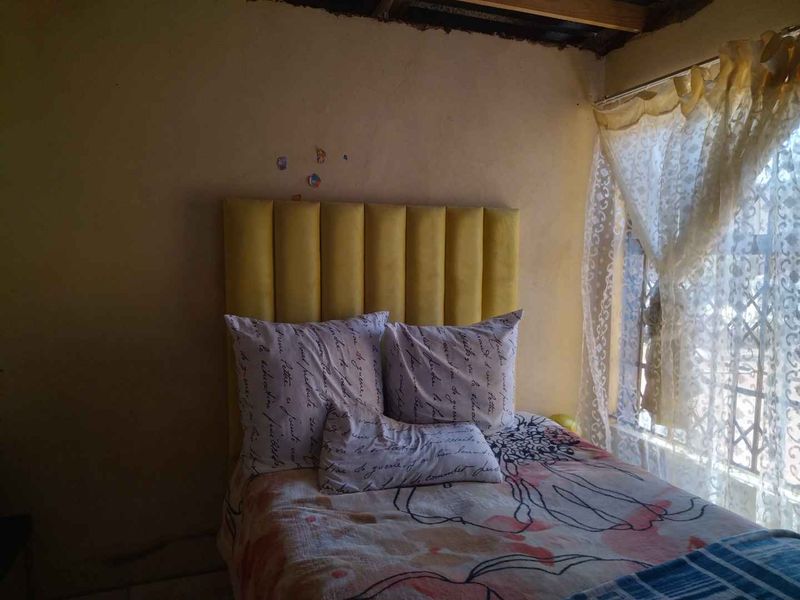 A bedroom featuring exposed ceiling beams and a security gate on the window, requiring cosmetic updates to the walls and ceiling.