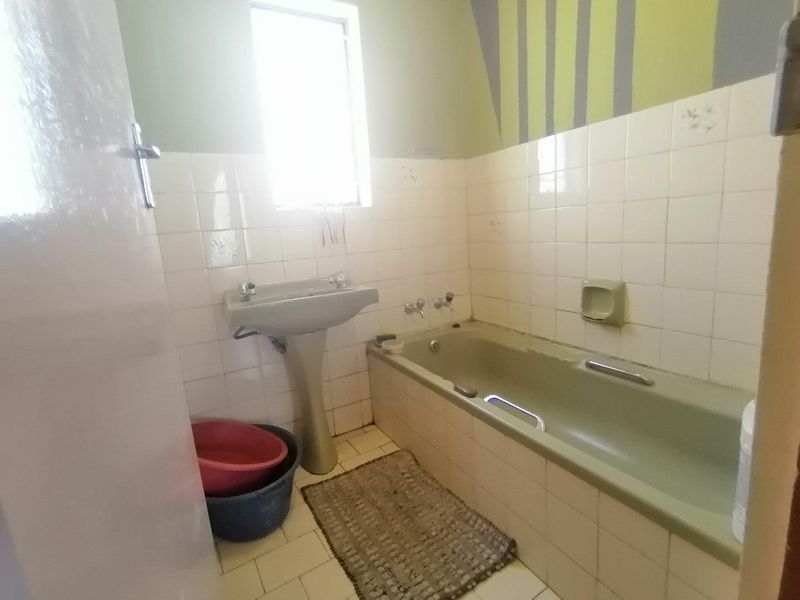 A dated bathroom featuring a pedestal basin and bathtub with tiled walls and flooring, offering significant potential for modernization and renovation.