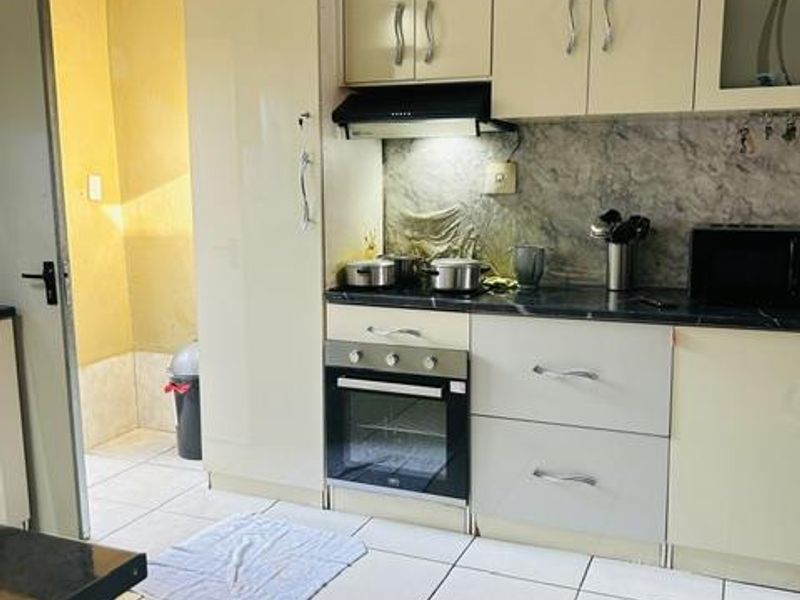 A functional kitchen featuring built-in cabinetry, an integrated oven, extractor fan, and tiled flooring with a stone countertop and backsplash.