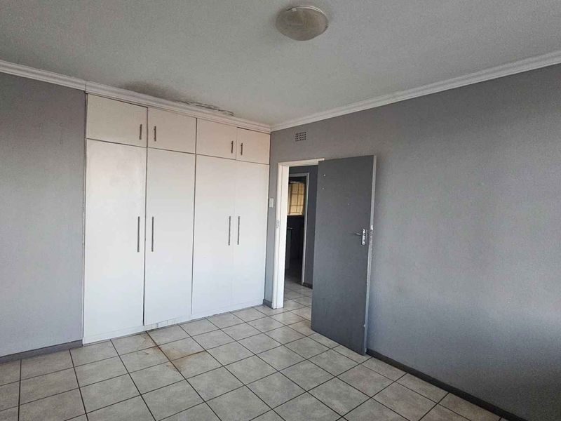 An empty bedroom featuring tiled flooring and built-in cupboards, showing signs of ceiling water damage and floor staining.