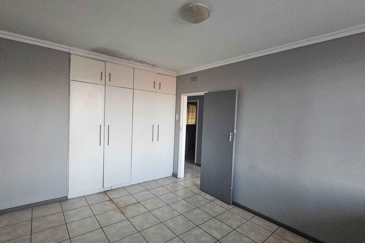 An empty bedroom featuring tiled flooring and built-in cupboards, showing signs of ceiling water damage and floor staining.