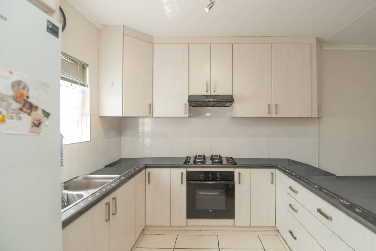 A functional U-shaped kitchen featuring light wood-grain cabinetry, dark countertops, a built-in oven, gas hob, and extractor fan with tiled flooring.