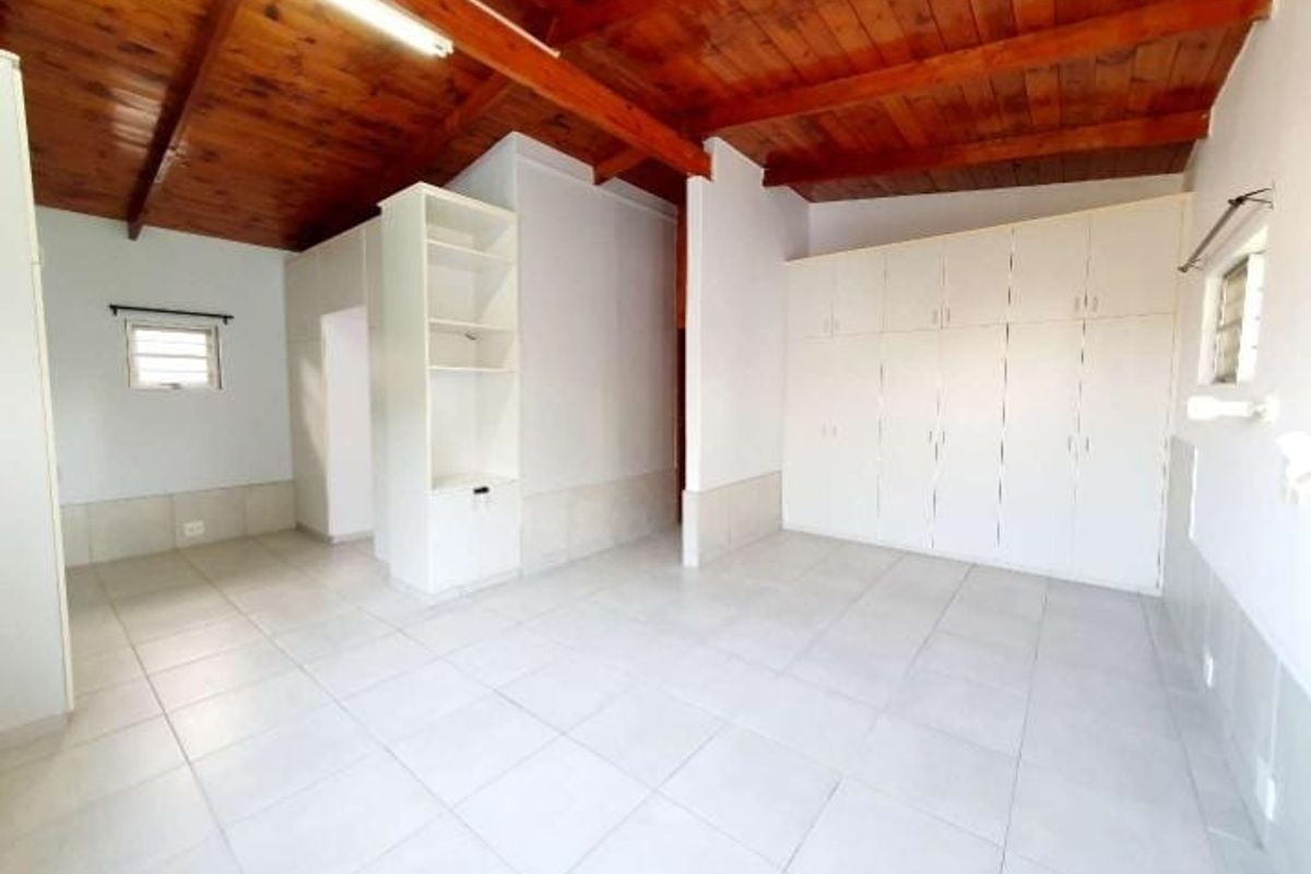 Spacious bedroom featuring high timber-beamed ceilings, tiled flooring, and extensive built-in wardrobe storage.