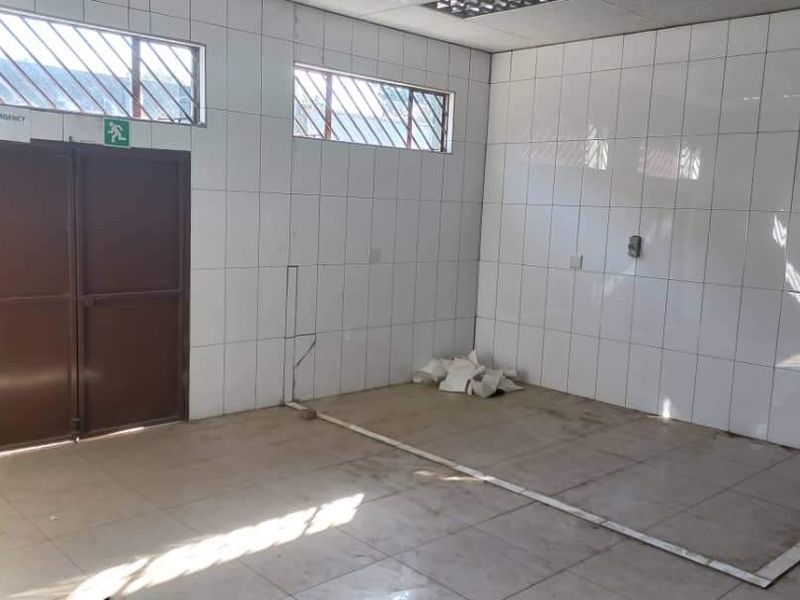 An empty industrial utility space featuring full-height wall tiling, tiled flooring, and secure metal access doors with high-level windows.
