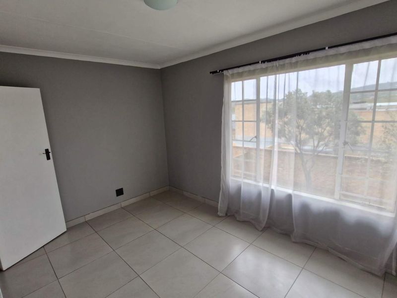 A bright and neutral bedroom featuring large windows with security bars, tiled flooring, and clean grey walls, offering a blank canvas for personalization.