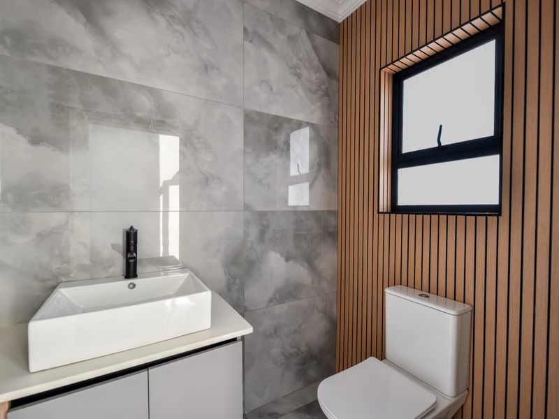 Modern bathroom featuring a vessel sink with black faucet, vanity cabinet, toilet, and stylish slatted wood wall paneling with large format marble-look tiles.