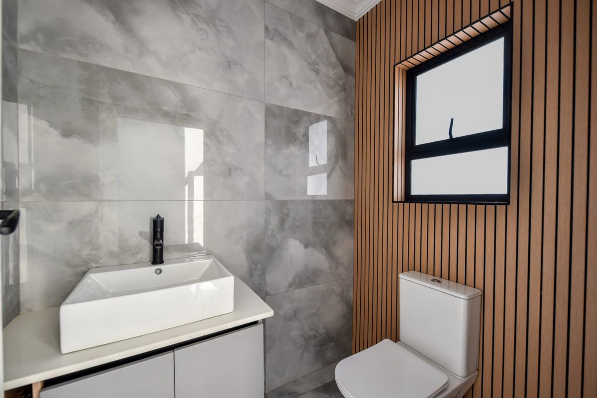 Modern bathroom featuring a vessel sink with black faucet, vanity cabinet, toilet, and stylish slatted wood wall paneling with large format marble-look tiles.