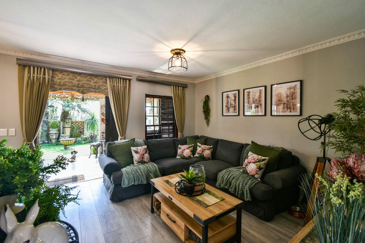 A comfortable living room featuring wood-look flooring, crown molding, and direct access to a covered patio and garden area through sliding doors.