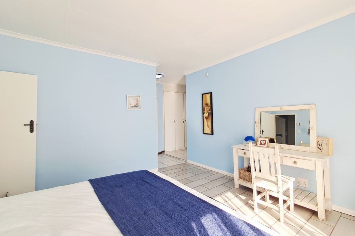 A bright bedroom featuring light blue walls, tiled flooring, and built-in cupboard storage, offering a clean and functional living space.