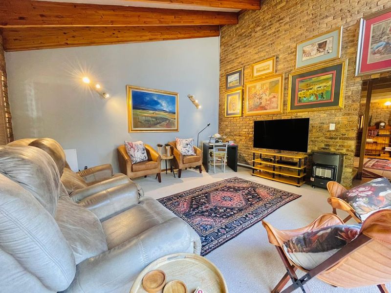 Spacious living room featuring a high vaulted ceiling with exposed timber beams and a prominent exposed brick feature wall.