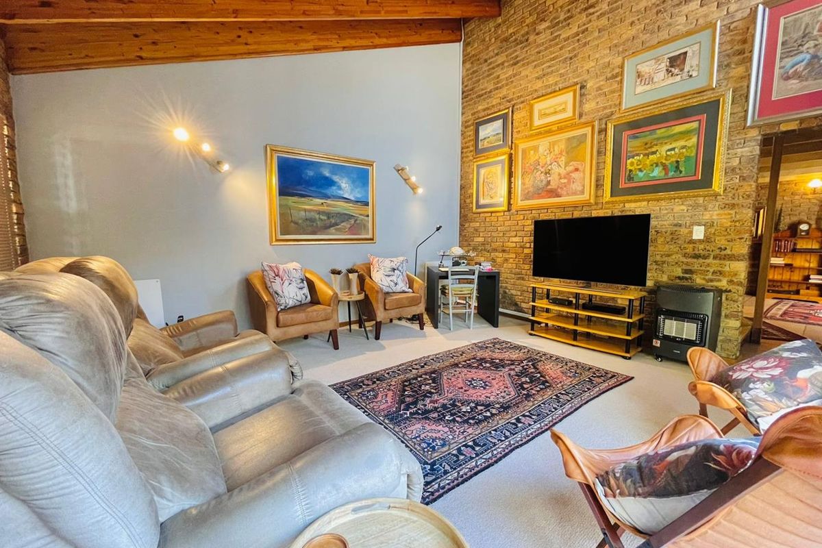 Spacious living room featuring a high vaulted ceiling with exposed timber beams and a prominent exposed brick feature wall.