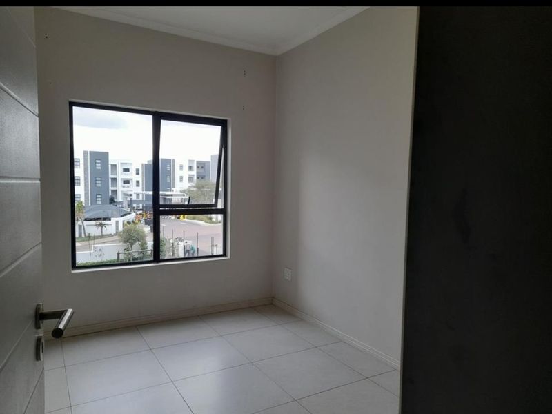 A bright, empty bedroom featuring neutral tiled flooring and a modern aluminium window frame, offering a clean and versatile space ready for personalization.