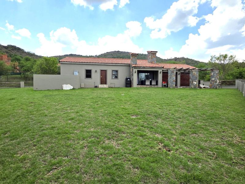 Rear view of a single-story house featuring a large lawn, stone-clad accents, terracotta roof tiles, and a timber pergola over the patio area.