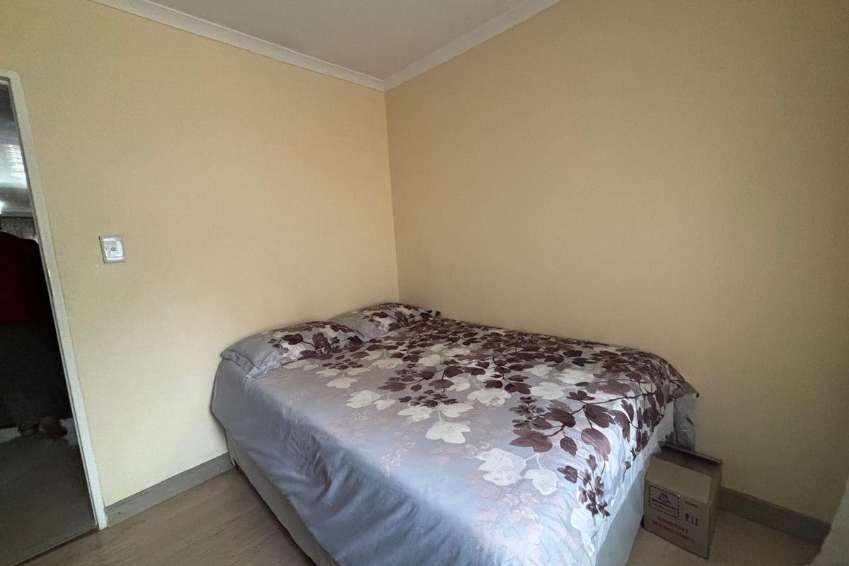 A simple bedroom featuring light-toned walls, coved ceiling cornices, and light-colored laminate flooring.