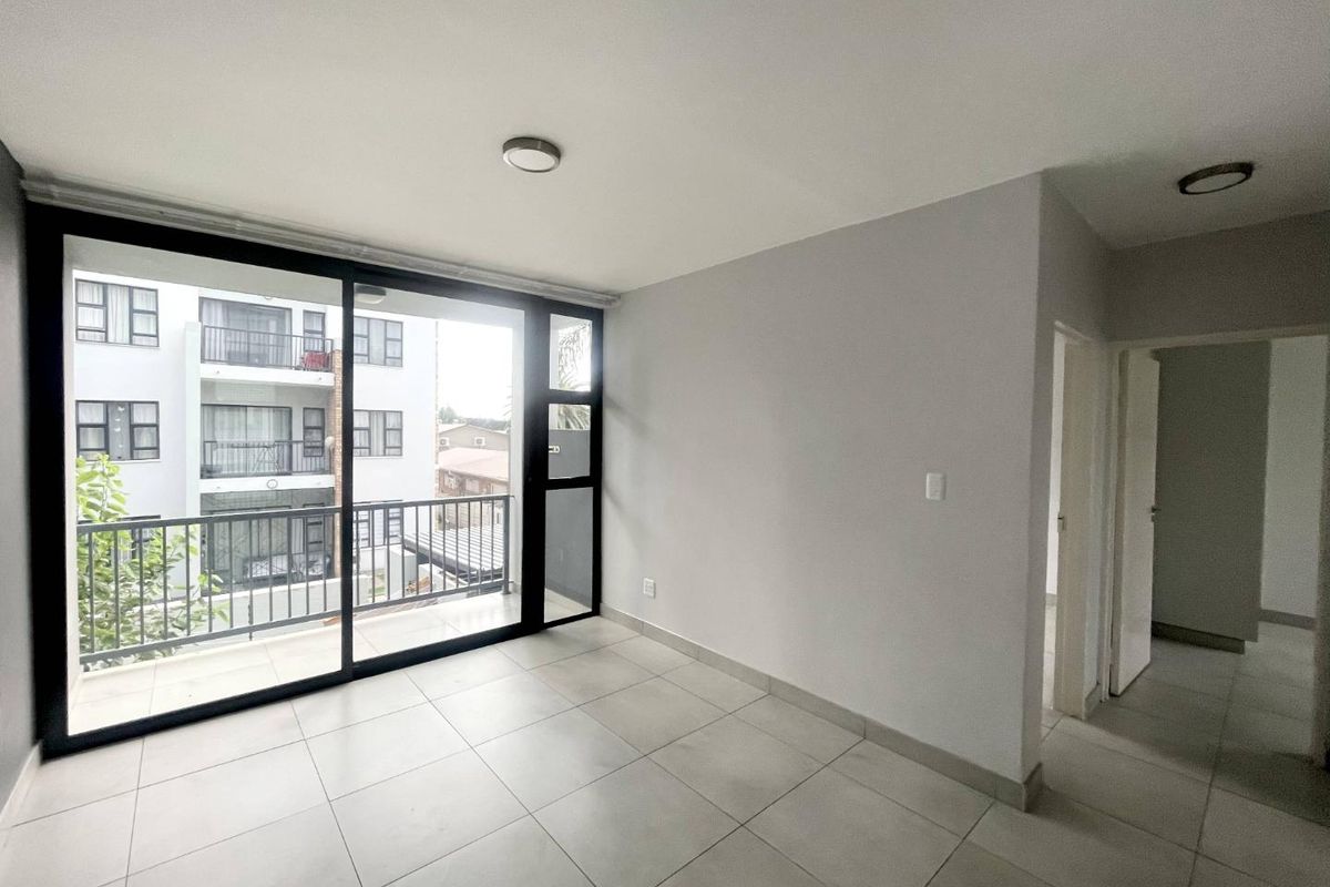 A bright, empty living area featuring large sliding glass doors that open onto a private balcony, with neutral tiled flooring throughout.