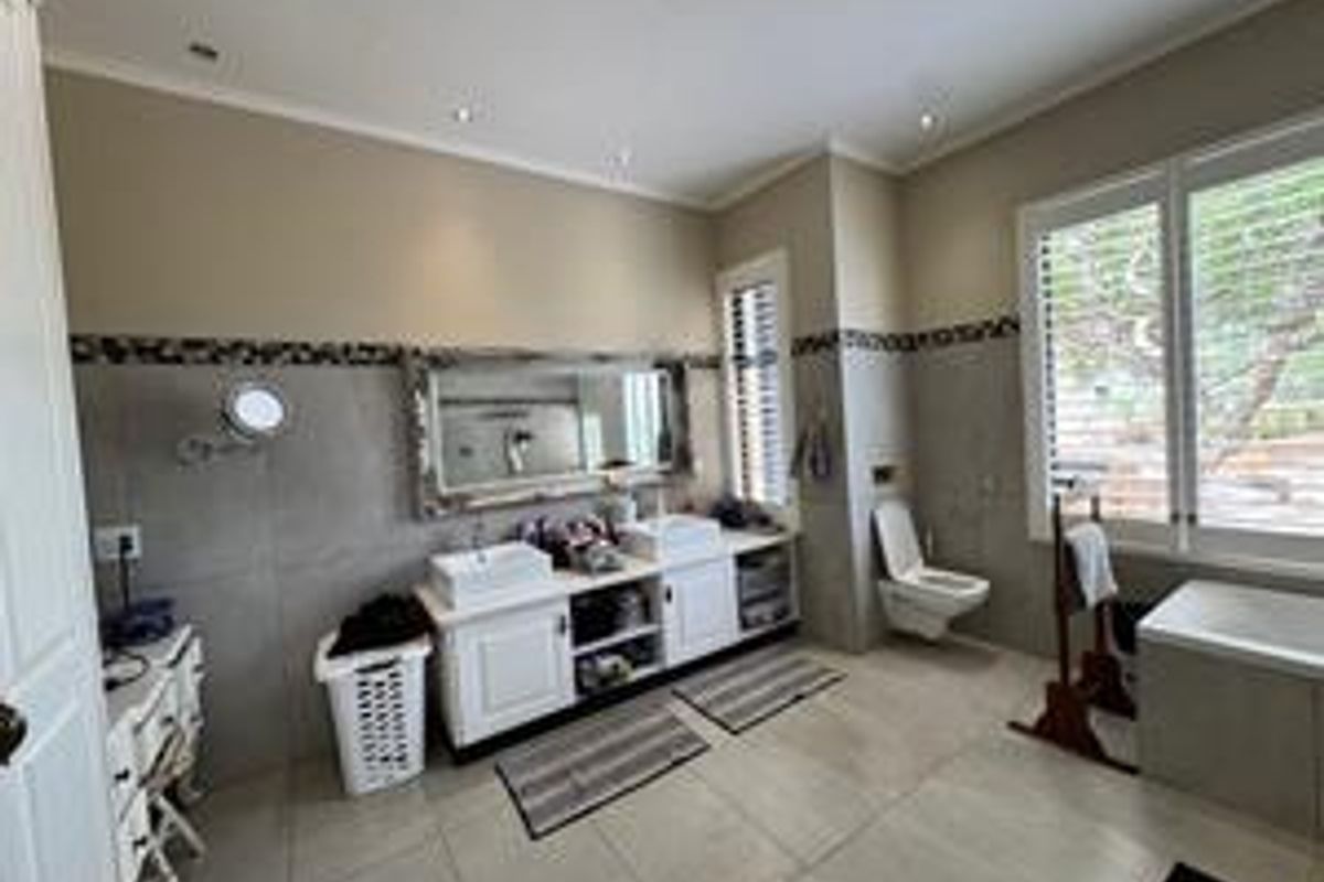 Spacious bathroom featuring a double vanity with vessel sinks, wall-mounted toilet, large window with shutters, and neutral tiled flooring and wall accents.