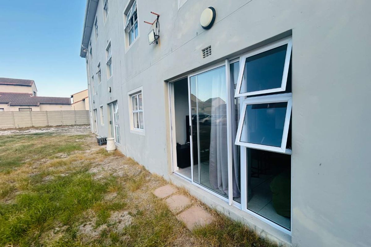 Exterior rear view of the apartment building featuring sliding glass doors, casement windows, and an adjacent open grass area.