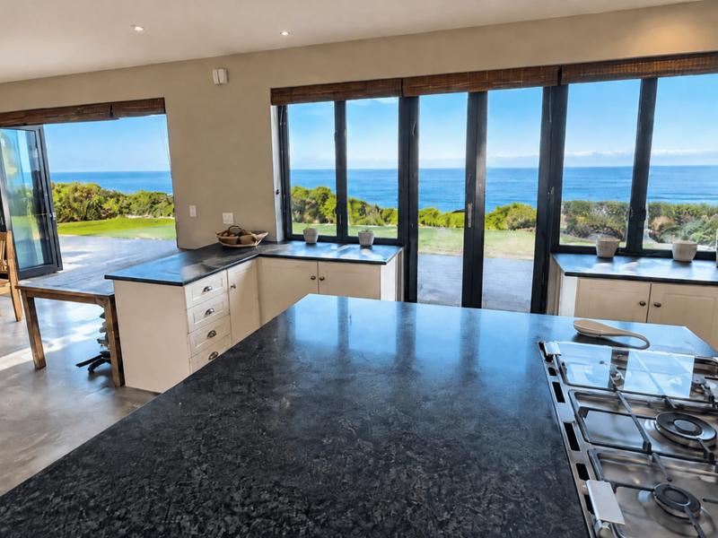 Spacious open-plan kitchen and dining area featuring a large granite island, gas cooktop, and expansive bi-fold doors opening to stunning ocean views.
