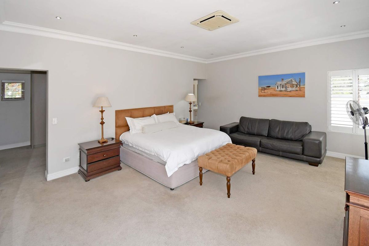 Spacious bedroom featuring neutral carpeting, recessed downlighting, and a built-in ceiling-mounted air conditioning unit with plantation shutters on the window.