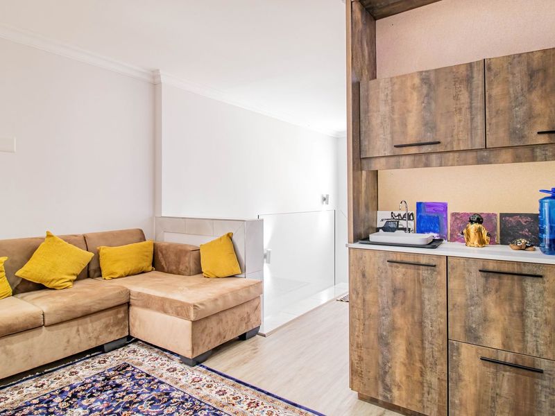A living area featuring laminate flooring, a glass balustrade, and built-in wooden cabinetry with an integrated sink.